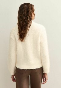 Suéter fuzzy color crema con un patrón texturizado, hombros caídos y puños acanalados; combinado con pantalones ajustados marrones.
