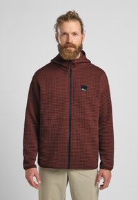 Braune, gesteppten Kapuzenjacke mit vollem Reißverschluss, die ein kleines Logo auf der Brust und elastische Bündchen hat. Der Stoff hat eine strukturierte Oberfläche.