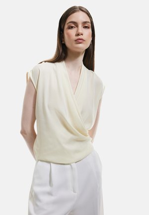 Blouse drapée jaune clair à manches courtes et design en V, associée à un pantalon blanc taille haute. Texture de tissu douce et lisse.
