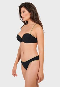 Svart underklädesset som består av en vadderad bh med guldfärgade remmar och matchande bikinitrosa, vilket betonar den släta tyget och väldefinierade former.