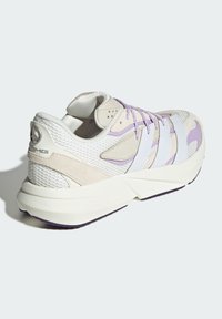 Sneaker z siateczkowej i zamszowej cholewą w jasnym beżu z fioletowymi akcentami. Posiada trzy białe paski po boku i teksturowaną podeszwę.