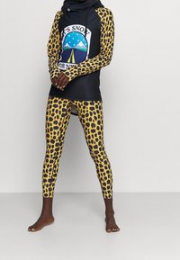 Bluza z kapturem w leopardzie wzory w czerni i żółci, zestawiona z pasującymi legginsami. Tkanina ma gładką strukturę i dopasowany krój.