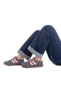 Zapatillas de ante gris con rayas y cordones rosas, con un detalle en el talón amarillo. Combinadas con unos vaqueros oscuros, remangados en los puños.