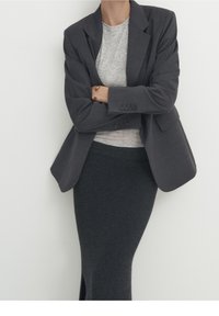 Blazer grigio con spalle strutturate, dettagli con bottoni e una gonna a maglia grigia texturizzata. T-shirt morbida, leggera e casual sotto.