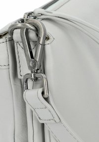 Chiusura in metallo argentato che collega la cinghia in pelle bianca all'angolo della borsa in pelle bianca, con cuciture visibili e superficie liscia.