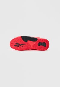 Κόκκινη και μαύρη σόλα παπουτσιού Reebok που εμφανίζει υφασμένο μοτίβο κράτησης και λογότυπο της μάρκας σε λευκό απλό φόντο.