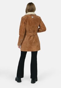 Abrigo de ante marrón con cuello de piel, cintura con cinturón y puños con cremallera, que presenta una textura suave y un diseño ajustado.