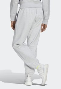 Vaaleanharmaat collegehousut, joissa on elastiset resorit, sivutaskut ja rento malli, yhdistettynä valkoisiin tennareihin, joissa on neonkorostuksia.