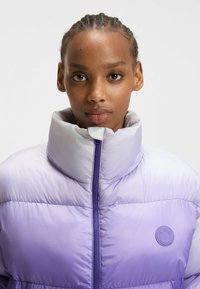 Lavendel puffer jakke med høj krave, lynlås lukning og struktureret overflade; har et cirkulært logoaccent på venstre bryst.