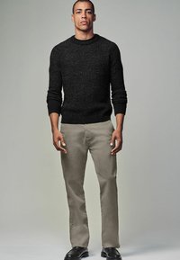 Schwarzer Strickpullover mit geripptem Rundhalsausschnitt und Bündchen, kombiniert mit hellbeigen Hosen und schwarzen Schuhen. Einfaches, figurnahes Design.