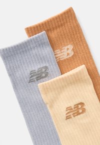 Τρία ζευγάρια ριγέ κάλτσες σε ανοιχτό μπλε, ανοιχτό κίτρινο και ανοιχτό πορτοκαλί, το καθένα με ένα διακριτικό λογότυπο σε αντίστοιχο χρώμα.