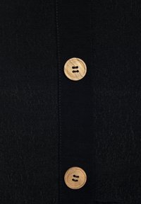 Schwarzes Stoffhemd mit glatter Textur, einer vertikalen Knopfleiste und zwei Holzknöpfen mit natürlicher Oberfläche, die zwei Knopflöcher zeigen.