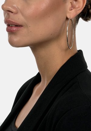 Silver hoop earring with a textured surface, featuring a thin, circular design. Displayed on a neutral background, with smooth skin visible.
