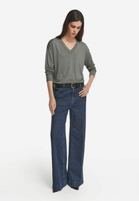 Grå v-ringad tröja med ribbade detaljer, tillsammans med högmidjade, vida blå jeans. Mörkt bälte ger kontrast; eleganta svarta skor.