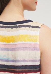 Mångfärgad ärmlös topp med horisontella ränder i nyanser av blått, gult, rosa och kräm, med en marinblå krage och textil med struktur.