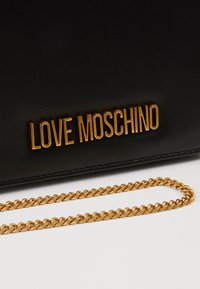 Czarny skórzany dodatek z złotym napisem "LOVE MOSCHINO" i pasującym złotym łańcuchem na białym tle.