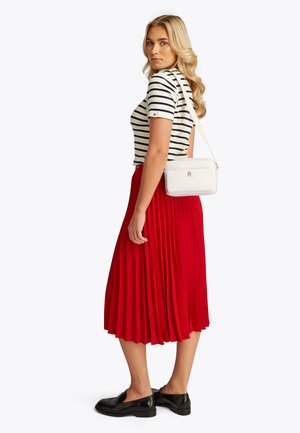 Geantă albă de umăr cu finisaj texturat, fustă plisată roșie și pantofi negri. Bluza are dungi orizontale albastre închise și albe.