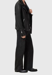 Giubbotto da biker in pelle nera con hardware argentato, tasche con zip e una vestibilità attillata, abbinato a pantaloni in denim nero a gamba larga e stivali alla caviglia.