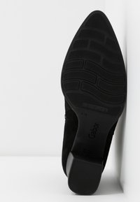 Semelle de chaussure noire à bout pointu avec une bande de roulement texturée, un talon bloc, et le nom de la marque "Gabor" visible en dessous.
