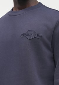 Námořnicky modrá mikina z bavlněné směsi s žebrovaným kulatým výstřihem a vyvýšeným vyšívaným logem na levé straně hrudi. Hladká textura.