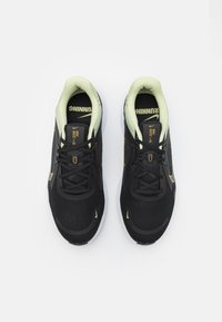 Chaussures de sport noires avec tige en maille, accents jaunes et surface texturée. Dispose de lacets noirs et d'un intérieur rembourré vert clair.