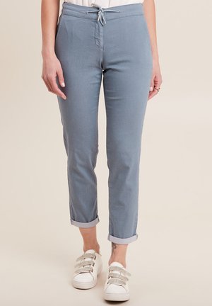 Lichtblauwe, taps toelopende broek met een elastische tailleband, opgerolde boorden en een gladde textuur. Gecombineerd met witte sneakers met drie banden.