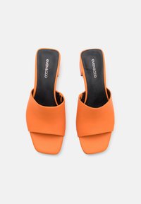 Sandalias deslizantes abiertas en la parte delantera de color naranja con un acabado liso y mate, y una amplia correa en la parte superior. Presenta un tacón bajo y cuadrado.