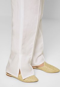 White, wide-leg trousers with side slits, paired with beige woven slip-on shoes featuring a pointed toe and flat sole.