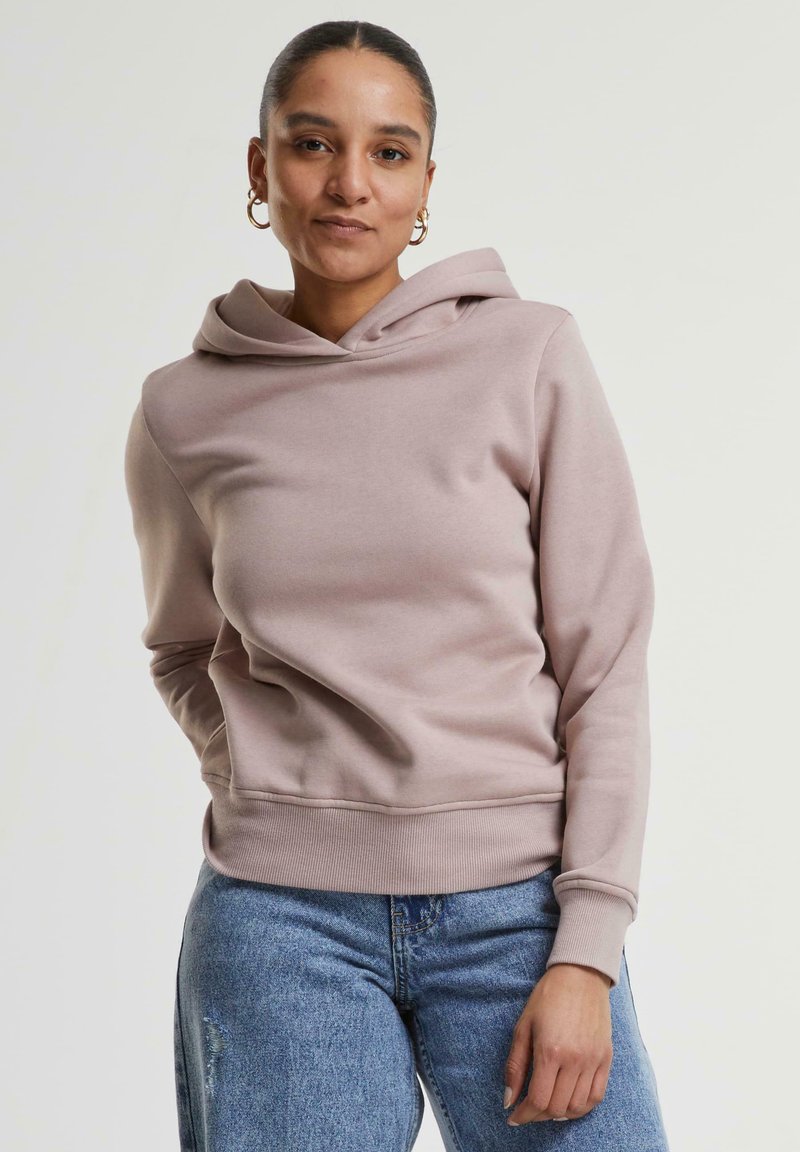 Hoodie rose clair en tissu doux avec une coupe décontractée, doté d'une grande capuche et de poignets et d'un ourlet côtelés. Associé à un jean en denim bleu.