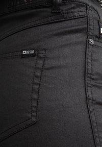 Mustad denim teksad, millel on sile tekstuur, kitsas lõige ja väike ristkülikukujuline „BIG STAR” silt ees taskul.