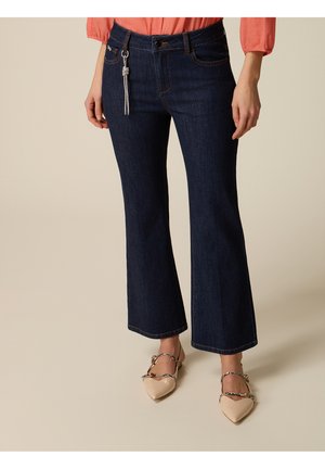 Donna che indossa jeans a zampa blu scuro con una camicetta corallo e ballerine beige con cinturini intrecciati.