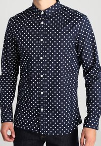 Navy blouse met witte stippen, lange mouwen en een klassieke kraag. Heeft een gladde textuur en een reguliere pasvorm.