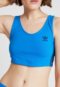Blå bomullstop med rund halsringning och broderad svart Adidas-logga. Inkluderar svarta randiga detaljer på sidorna.