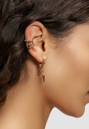 Goldene Ohrringe mit Stacheldesign, mehreren Creolen und Kettenakzenten, getragen an einem Modell mit lockigem Haar.