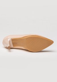 Zapato de tacón alto de charol beige con punta afilada. La suela tiene una textura con un patrón de diamantes. Presenta un lazo decorativo en la parte trasera.
