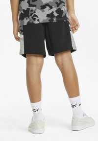 Pantaloni sportivi neri con accenti grigi sui lati, una texture liscia, abbinati a calze bianche e scarpe da ginnastica grigie con un accento dorato.