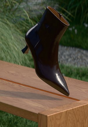 Botte chelsea noire brillante à bout pointu avec un petit talon reposant sur le bord d'un banc en bois en extérieur, avec de l'herbe en arrière-plan.
