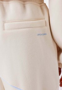 Beige sweatshirt met een gestructureerde afwerking, een klein blauw logo en een discreet achterzakje voor opberging.