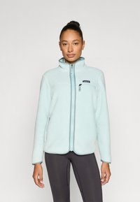 Γαλάζιο μπουφάν από φλίς με ψηλό γιακά, πλήρης φερμουάρ και τσέπη στο στήθος με φερμουάρ. Απαλή υφή, μακριά μανίκια με ελαστικές λεπτομέρειες.