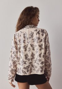 Beige blouse with a collar, featuring silver sequin floral patterns. Soft fabric, long sleeves, and a relaxed fit; back view shown.