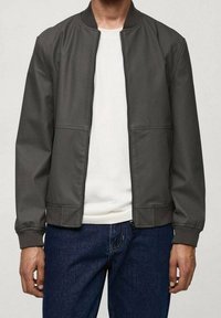 Chaqueta bomber gris de tela lisa, con cremallera frontal, puños acanalados, dos bolsillos delanteros y una camiseta blanca lisa debajo.