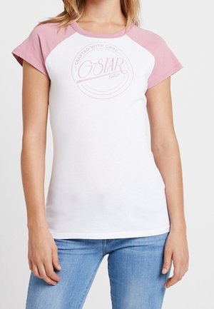 Kvinde iført en hvid t-shirt med pink ærmer og "G-STAR RAW" logo, parret med lyseblå jeans, stående mod en ensfarvet baggrund.