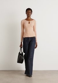 Top de manga larga de color rosa claro con diseño de canalé y corte en forma de llave, combinado con unos vaqueros de pierna ancha de color azul oscuro. La modelo sostiene un bolso negro.