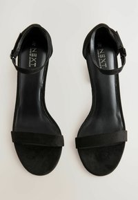 Sandales à talon haut en daim noir avec une fine bride de cheville et une large bande frontale. Texture lisse avec un intérieur poli et un design de bout arrondi.
