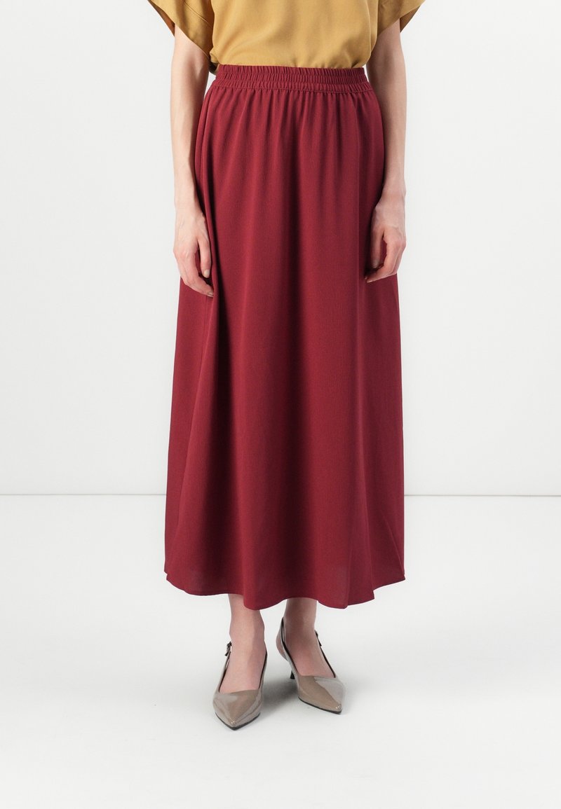 Jupe longue bordeaux avec une taille élastique et des poches latérales, en tissu doux, associée à des escarpins beiges à bouts pointus.