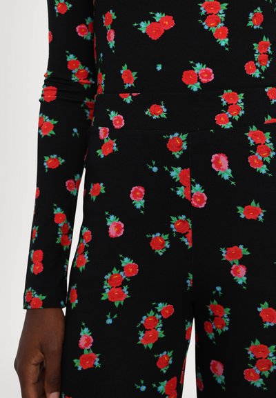 Tissu noir avec un motif floral comportant des roses rouges et des feuilles vertes. Manches longues avec un design ajusté et une texture lisse et extensible.