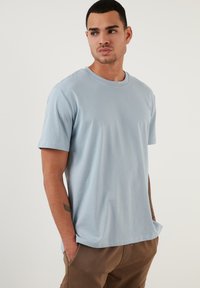 Tricou din bumbac de culoare albastru deschis, cu mâneci scurte și guler rotund; are o croială relaxată și o textură netedă, potrivit pentru îmbrăcăminte casual.