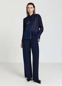 Marineblaue, durchsichtige Knopf-Up-Bluse mit vertikalen Streifen, langen Ärmeln und klassischem Kragen, kombiniert mit weit geschnittenen marineblauen Hosen.