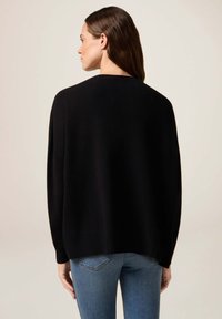 Svart oversized tröja med långa ärmar, ribbat avslut, slät textur, bärs med ljusblå jeans, sedd bakifrån.