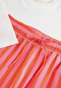 Bavlněný dvoudílný outfit s krátkými bílými rukávy a sukní s pruhy v růžové a oranžové barvě, opatřenou elastickým pasem a mašlí.
